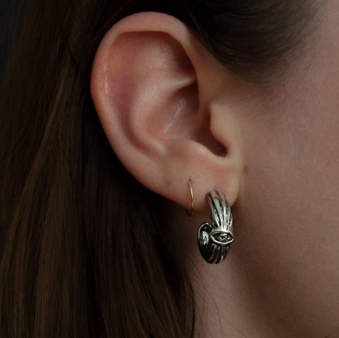 Everyday wear earrings shown on woman's ear. Silver hoop with an esoteric symbol, a hand carved eye. 