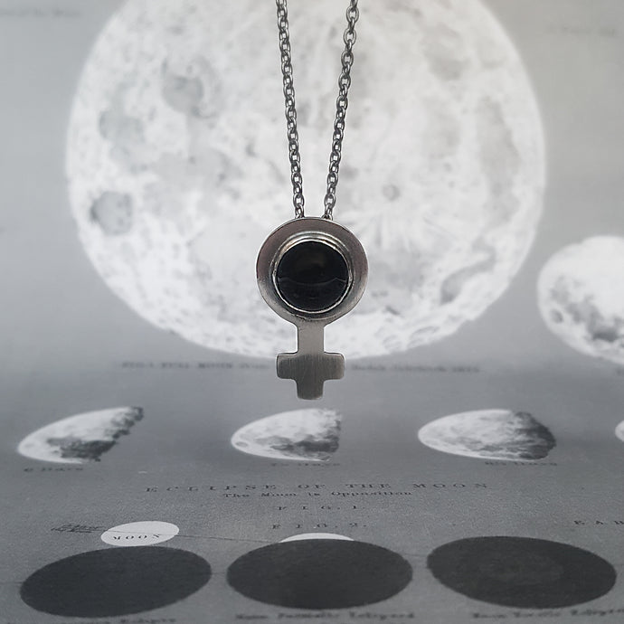 Feminist symbol necklace in silver, with a round onyx. On a background of the moon.