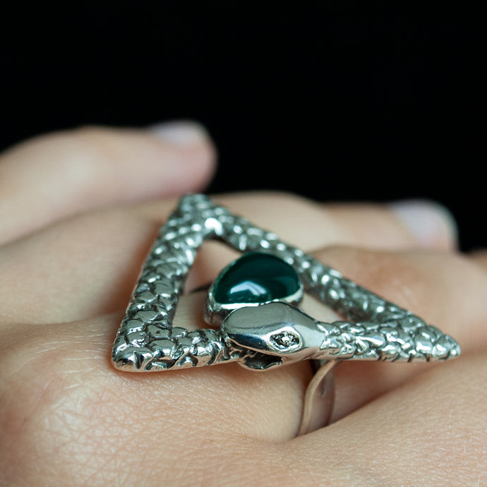 Close up of a hand wearing a hand carved snake ring in the shape of a triangle ouroboros, surrounding a pear-shaped green agate.