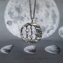 Load image into Gallery viewer, Moon and star necklace in round shape, made of silver. Shown on a background of the moon.