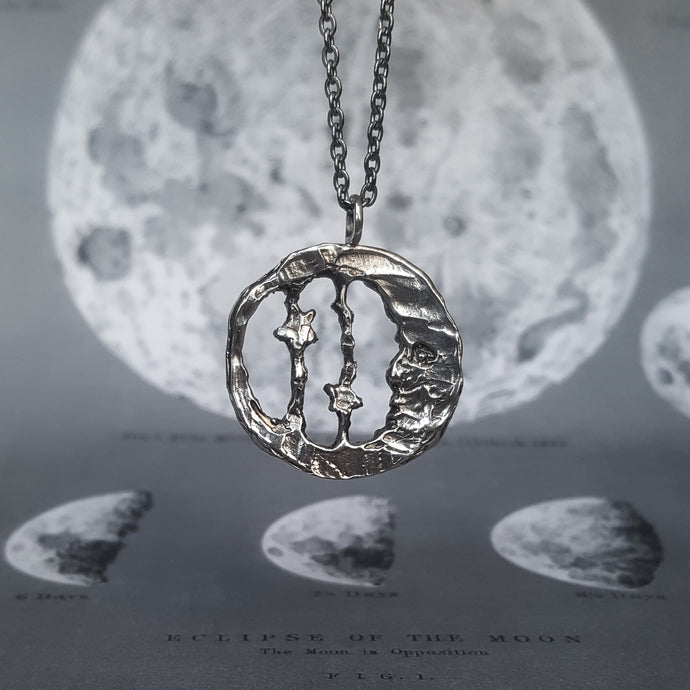 Moon and star necklace in round shape, made of silver. Shown on a background of the moon.