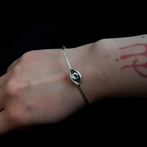 Thin silver bangle with an esoteric symbol, a hand carved eye. Shown on a woman's wrist