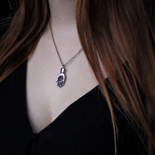 Load image into Gallery viewer, Silver necklace in the shape of a hand with an eye in the palm. Hanging around the neck of a woman.