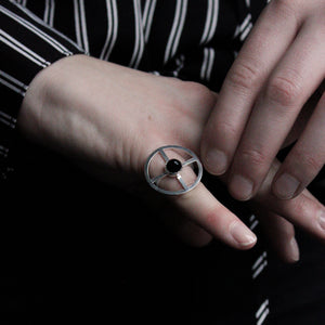 Silver ring shaped as a sun cross, with black onyx, worn on pinky finger.